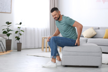 Wall Mural - Man suffering from hemorrhoid in living room. Space for text