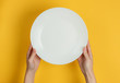 © splitov27 - Female hand holds empty white plate on yellow background. Top view.