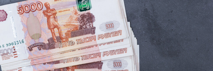 Big stack of Russian money banknotes of five thousand rubles lying on a grey cement background.