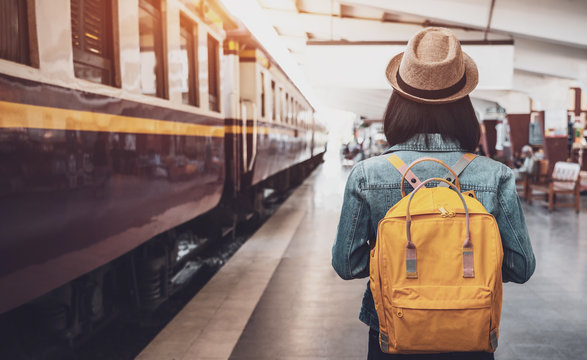 Fototapete - Young asian woman traveler with backpack in the railway, Backpack and hat at the train station with a traveler, Travel concept. Woman traveler tourist walking at train station