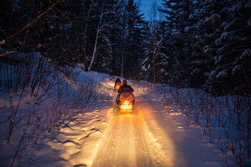 snowmobile in the evening goes through the winter forest. headlights. night road through the winter forest. snowmobile at night