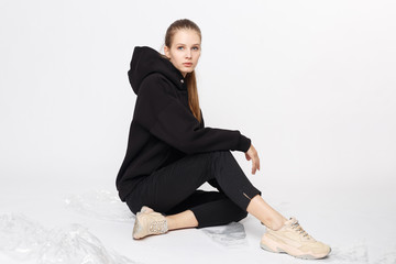 Wall Mural - Young girl wearing blank and oversize black long hoody and balck jeans pants . Sitting on white background. Isolated.