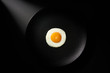 Fried egg in black ceramic plate on black background. Top view. Copy space.