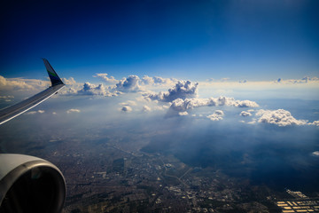 looking out the window of an airplan to see a wingtip, engine and bright fluffy clouds and a deep bl