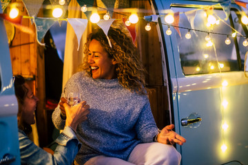 Alternative travel and celebration concept with couple of people adult cheerful happy women celebrate together in a vintage van camper  and party lights outdoor