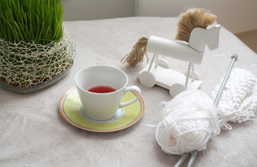 Cup of tea on the fluffy blanket surface with green plants, wooden horse toy and white wool knitwear. Happy home concept