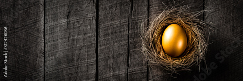 Fotografía Banner Of Golden Nest Egg On Rustic Wooden Table Background - Investment Concept