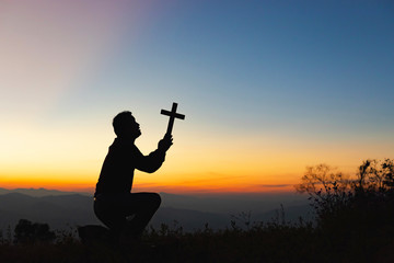 Wall Mural - Human praying and holding christian cross for worshipping God at sunset sky background.Christian, Christianity, Religion copy space background.