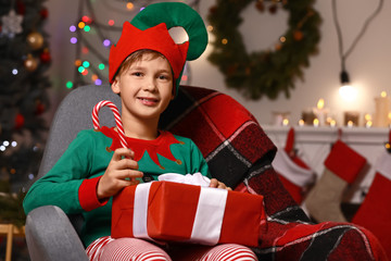 Sticker - Little boy in costume of elf, with gift and candy cane in room decorated for Christmas