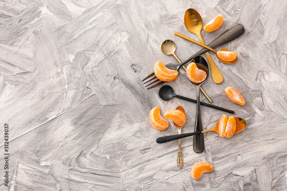 Sweet tangerine segments, spoons and forks on grey background