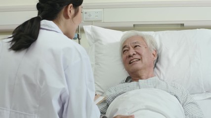 Wall Mural - friendly young asian female doctor talking to male senior patient at bedside in hospital ward