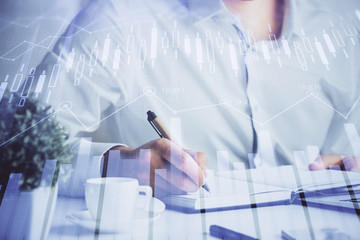 Double exposure of man's hands writing notes of stock market with forex chart.