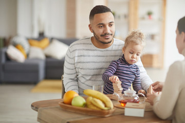 Portrait of caring mixed-race father playing with cute daughter while enjoying family breakfast at home, copy space