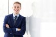 © moodboard - Portrait of smiling young businessman with arms crossed leaning on wall at office