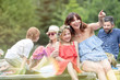 © MDBPIXS - Smiling woman pointing to daughter while sitting on pier against family at lakeshore during summer