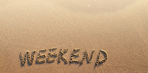 The word weekend written on sand. Summertime concept.