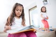 © moodboard - Cute girl reading book with sister playing in background at home