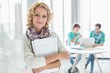 © MDBPIXS - Portrait of creative businesswoman holding files with colleagues working in background at office