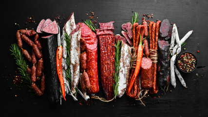 Wall Mural - Assortment of sausages, salami and fuet. Dried and smoked salami on black wooden background. Top view.