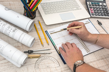 Male hands writing on notepad with part of industrial blueprint with calculator, tools and laptop