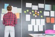 © MDBPIXS - Rear view of businessman analyzing documents on wall at creative office