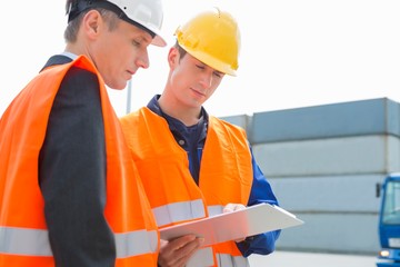 Workers discussing over clipboard in shipping yard