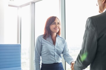 Wall Mural - Smiling businesswoman shaking hands with businessman in office