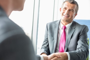 Wall Mural - Smiling mature businessman shaking hands with partner in office