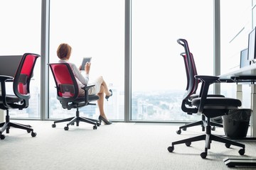 Wall Mural - Full length of young businesswoman using tablet PC on chair in office