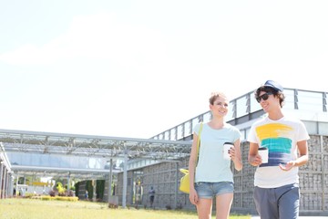 Wall Mural - Smiling couple holding disposable cups while walking at park