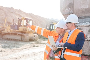 Wall Mural - Supervisor showing something to coworker holding laptop at construction site