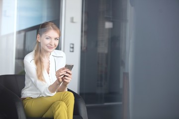 Portrait of confident young businesswoman using mobile phone on chair in office