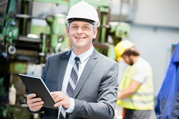 Wall Mural - Portrait of confident mature businessman using digital tablet with worker in background at factory