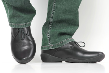 Men's legs in jeans and black classic shoes on white background