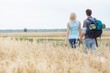 © moodboard - Rear view of young hiking couple walking through field