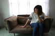 © Snowhite - Asian woman stressful face with her hands cover of face. Short hair asian Woman feel lonely and sad sit alone on sofa bed in the living room