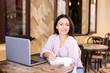 © dianagrytsku - Smiling woman in cafe using laptop and note some data on notebook