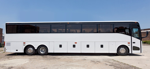 side view of parked white sightseeing tor bus under blue sky.