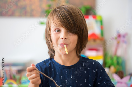 Fotografía Sweet preschool boy, eating spaghetti at home, making a mess and having fun