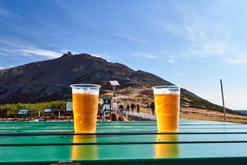 Plastic beer mugs with beer on the table against the background of the Sniezka mountain peak in Poland.