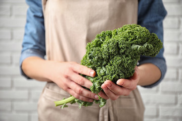 Woman holding fresh kale leaves near white brick wall, closeup