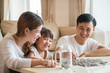 © tuastockphoto - Asian family teach Asian cute girl saving money putting coins into piggy glass bank, vintage tone. education, save money, Asian family, investment, future investment or family relationship concept