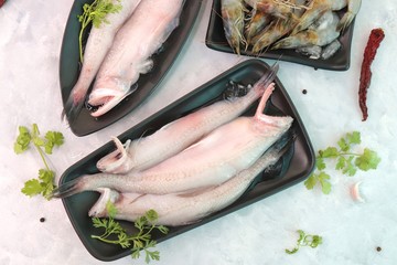 Fresh sea fish Bombay duck or Bombil and white prawns with ingredients for cooking, lemon, green coriander, black pepper, red chills and garlic. White background top view