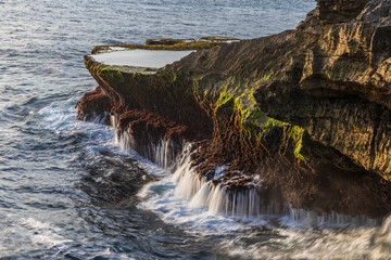 Wall Mural - Outcrop at Devil's Tear, on the shore of Nusa Lembongan island, Bali, Indonesia. Tide pool on top of the rocky cliff; water streaming from the rocks back into the ocean. 