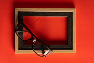 Spectacles and empty photo frame against red background