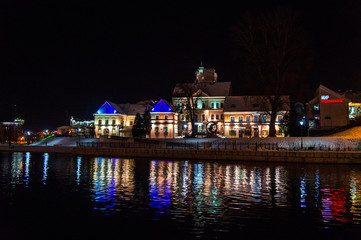 Christmas night neon glowing cityscape. Bright city lights reflected in the water. Minsk Belarus. December 31 2019