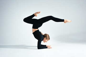 Young handsome fit woman wearing black sportswear doing stretching body against white background. Studio shot. Flexible girl doing yoga poses in white room