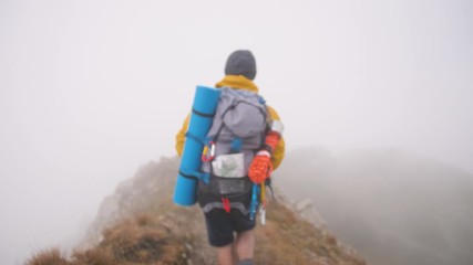 Wall Mural - young man hiker on mountain with cloudy sky and fog. yellow jacket, backpack and beanie. traveling d