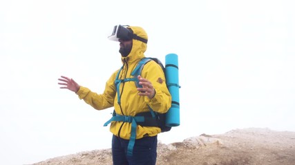Wall Mural - vr virtual reality headset. young man hiker moving hands on cloudy sky and fog background. yellow ho