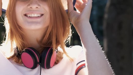 Wall Mural - Portrait of pretty positive teenage girl with red hair wearing straw hat and pink earphones smiling happily in camera.